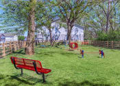 Thumbnail 27 of 53 - a park with a red bench and kids playing in the grass at The Dylan, Murfreesboro, TN 37129
