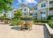 Thumbnail 47 of 48 - A patio with chairs and an umbrella in front of apartment buildings.at Century Hampton Roads, Virginia, 23435