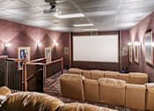 Thumbnail 11 of 24 - A row of brown leather seats are arranged in front of a large screen in a theater room at Ridge Crossings Apartments, Hoover, AL 35244