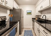 Thumbnail 9 of 18 - A kitchen with a black counter top and a fridge.