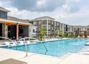Thumbnail 33 of 36 - A large swimming pool with lounge chairs and a building in the background.