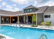 Thumbnail 32 of 36 - A large swimming pool in front of a house with a patio and lounge chairs.