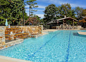 Thumbnail 9 of 24 - A large swimming pool with a stone wall and a small gazebo in the background.