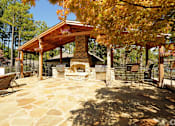 Thumbnail 6 of 24 - A patio with a fireplace and a table surrounded by trees.