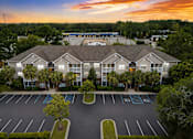 Thumbnail 19 of 20 - A parking lot in front of a building with trees and a sunset in the background.