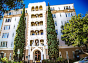 Thumbnail 1 of 13 - A tall building with a large arched doorway and balconies on the upper floors.