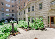 Thumbnail 12 of 39 - Courtyard area at Park Lane Villa apartments fitted with tiled walkway, greenery, and water fountain.