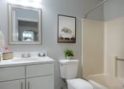 Thumbnail 7 of 8 - a small bathroom with a white vanity and toilet next to a white bathtub with a shower