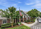 Thumbnail 18 of 42 - Brick clubhouse entrance with american flag and landscaping at Alden Place at South Square Apartments, Durham, 27707