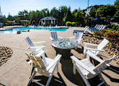 Thumbnail 5 of 30 - A poolside area with white chairs and a table.