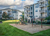 Thumbnail 26 of 30 - A playground area with a slide, swings, and a seesaw in front of apartment buildings.