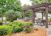 Thumbnail 19 of 26 - A wooden pergola with a sign on it is surrounded by greenery and a picnic table.