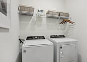 Thumbnail 9 of 18 - A laundry room with a washer and dryer and a shelf with baskets and a handbag. at Arcadia Cartersville Apartments, Cartersville, GA