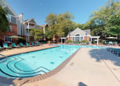 Thumbnail 13 of 36 - a swimming pool with lounge chairs and umbrellas in front of a brick building at Autumn Park Apartments, North Carolina