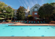 Thumbnail 16 of 36 - a swimming pool with lounge chairs and umbrellas in front of a brick building at Autumn Park Apartments, North Carolina