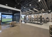 Thumbnail 21 of 41 - a gym with a large screen on the wall and exercise equipment at Deca Apartments, South Carolina