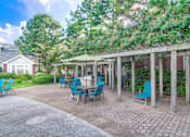 Thumbnail 11 of 22 - A patio with blue chairs and a table is surrounded by trees at Enclave at Wolfchase Apartments, Memphis