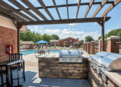 Thumbnail 16 of 21 - a patio with a grill and a swimming pool with umbrellas at Brightwaters Apartments, Little Rock, AR