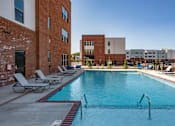 Thumbnail 18 of 21 - A pool surrounded by chairs and buildings.