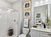 Thumbnail 7 of 43 - A white bathroom with a toilet, sink, mirror, and framed artwork.