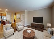 Thumbnail 5 of 15 - A living room with a white couch, a coffee table, and a television.