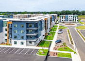 Thumbnail 27 of 29 - A large apartment complex with a parking lot in front.