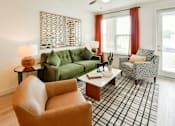 Thumbnail 7 of 29 - A living room with a green couch, a brown chair, and a black and white plaid area rug