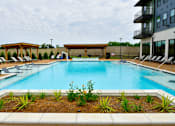 Thumbnail 11 of 29 - A large swimming pool surrounded by a concrete border and a small garden in the foreground.