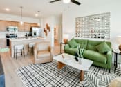 Thumbnail 6 of 29 - A living room with a green couch, a coffee table, and a kitchen area in the background.