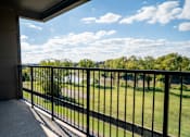 Thumbnail 32 of 37 - A balcony with a black railing overlooks a green lawn and trees at Harbor Side at Conwood Flats Apartments in Uptown Memphis, TN