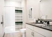 Thumbnail 7 of 37 - A bathroom with a toilet, sink, and shower curtain at Harbor Side at Conwood Flats Apartments in Uptown Memphis, TN