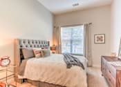 Thumbnail 4 of 14 - A bedroom with a large bed, a nightstand with a clock, a dresser with a mirror, and a window with curtains at Highland Row Apartments, Tennessee