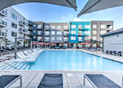 Thumbnail 5 of 14 - A large outdoor swimming pool surrounded by lounge chairs and umbrellas at Highland Row Apartments, Memphis, Tennessee