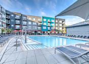 Thumbnail 8 of 14 - A swimming pool area with sun loungers and a building in the background at Highland Row Apartments, Tennessee