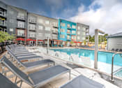 Thumbnail 7 of 14 - A pool area with sun loungers and a building in the background at Highland Row Apartments, TN, 38111