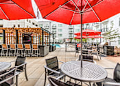 Thumbnail 9 of 14 - A patio with red umbrellas and chairs at Highland Row Apartments, Memphis
