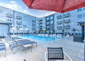 Thumbnail 6 of 14 - A pool area with sun loungers and a red umbrella.
