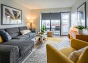 Thumbnail 8 of 38 - A grey couch with yellow pillows sits in a living room with a large window.at Iris Luxury Apartments, Memphis  