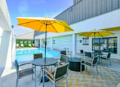 Thumbnail 38 of 38 - A poolside area with a table and chairs under a yellow umbrella.
