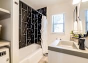 Thumbnail 26 of 28 - A bathroom with a bath tub and dark tyle with a window and modern sink at Kiwi Goji Apartments, Tennessee, 38111