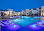Thumbnail 1 of 25 - A swimming pool with blue and purple lights in front of a building.