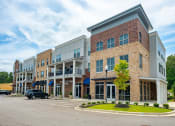 Thumbnail 20 of 21 - Lakeland, TN Apartments Near Wolfchase Galleria - Lakeland Town Square - Property EXteiror with Brick Details, Balconies, White Trim, with Parking View, and Nearby Landscaped Greenery