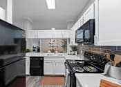 Thumbnail 5 of 48 - Modern kitchen with black appliances and white cabinets at The Ambrose, Texas, 77040