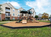 Thumbnail 14 of 16 - A playground with a slide and sandbox in front of apartment buildings at The Fenwick Apartments, Humble, TX