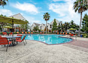 Thumbnail 3 of 16 - A pool surrounded by chairs and umbrellas with houses in the background at The Fenwick Apartments, Texas