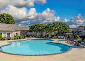 Thumbnail 18 of 28 - A large outdoor swimming pool surrounded by a concrete patio and a grassy area with trees.