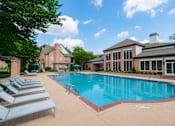 Thumbnail 14 of 30 - A large swimming pool surrounded by lounge chairs and a building in the background.