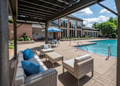 Thumbnail 15 of 30 - A patio with a couch and chairs under a roof next to a pool.