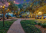 Thumbnail 27 of 30 - A park with a walkway, benches, and trees is lit by street lamps.