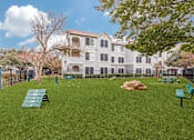 Thumbnail 24 of 30 - A large grassy area with benches and a building in the background.